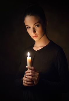 a woman holding a lit candle in her hands with the light shining on her face