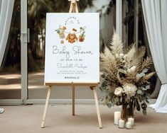 a baby shower sign next to a bouquet of flowers and candles in front of an open door