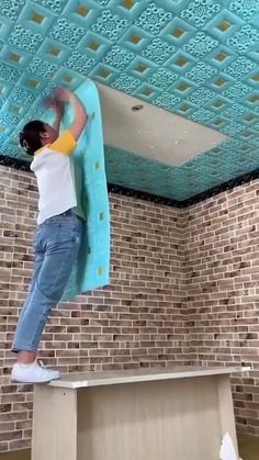 a woman standing on top of a wooden table under a blue painted ceiling above a brick wall