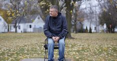 a man sitting on top of a chair in the middle of a field with leaves