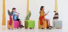 two children sitting on colorful chairs in front of a white wall