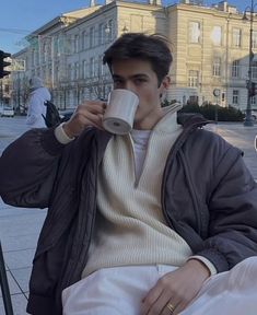 a man drinking from a cup while sitting on a bench in front of a building