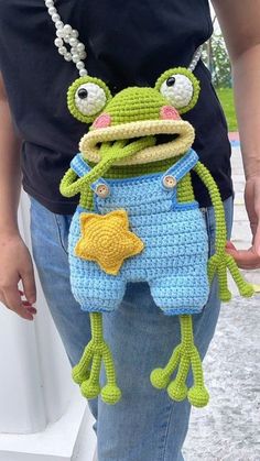 a crocheted frog holding onto a handbag