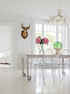 a dining room table with clear chairs and vases on it's end tables