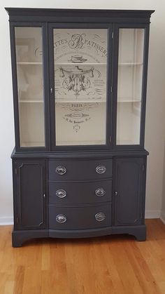 a black china cabinet with glass doors and drawers on the bottom, in front of a white wall