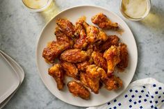 a white plate topped with chicken wings next to two glasses of beer and napkins