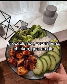 a person holding a plate with chicken, rice and cucumbers on it that says broccoli, rice, cucumbers, chicken, guacamole