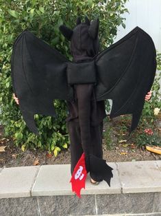 a young boy dressed up as a bat with wings and tail, standing on the sidewalk