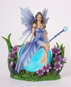 a fairy figurine sitting on top of a blue ball with purple flowers around it