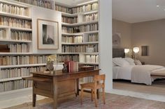 a room filled with lots of books and furniture next to a bed covered in white sheets