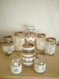 many jars are lined up on a table with lace doily and pearls in them