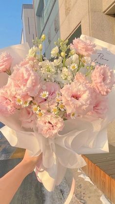 a bouquet of pink and white flowers is being held up by someone's hand