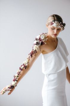 a woman in a white dress with flowers on her arm and one hand holding something