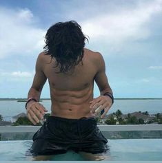 a shirtless man sitting on top of a surfboard in the water with his hands behind his back