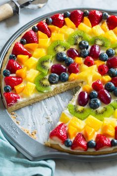 a fruit pizza on a pan with one slice cut out and ready to be eaten