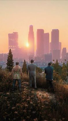 three people standing on top of a hill looking at the sunset in front of some tall buildings