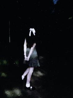 a woman with bunny ears is standing in the dark, wearing a dress and white socks