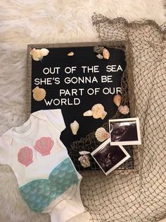 baby clothes and other items are laid out on a white furnishing with the words, out of the sea she's gone be part of our world