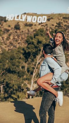 a man carrying a woman on his back in front of the hollywood sign with trees