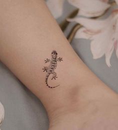 a small gecko tattoo on the left inner forearm and foot is shown in black ink