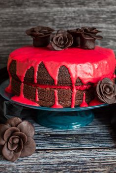 a cake with red frosting and chocolate flowers on top, sitting on a blue plate