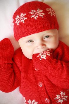 a baby wearing a red sweater and hat with white snowflakes on it's sleeves