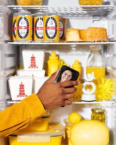 a person holding a cell phone in front of a refrigerator filled with food and condiments