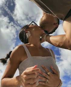 a man and woman kissing each other while standing under a blue sky with white clouds