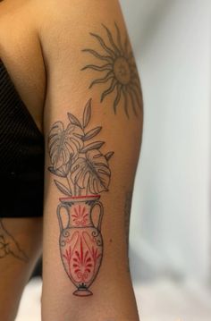 a woman's arm with tattoos on it and flowers in a vase behind her