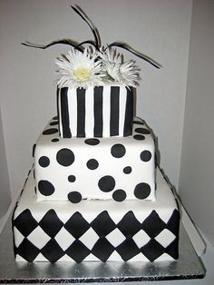 a three tiered cake with black and white designs on it, decorated with daisies