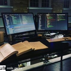 two computer monitors sitting next to each other on top of a desk covered in books