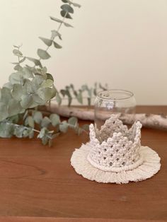 a crocheted crown sits on a table next to a vase with greenery