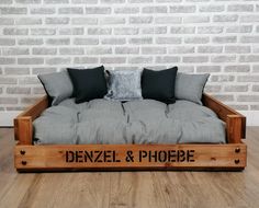 a couch made out of wooden pallets with pillows on the top and bottom, sitting in front of a brick wall