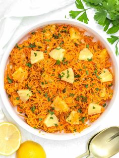 a white bowl filled with pineapple rice next to sliced lemons and parsley