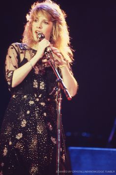 a woman in a black dress holding a microphone and singing into the microphone with her hand