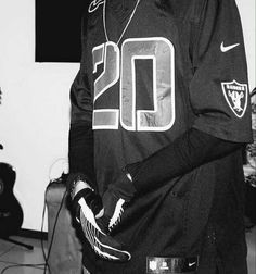 a young man with headphones on standing in front of a microphone and wearing an oakland football jersey