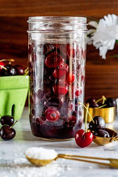 a jar filled with cherries sitting on top of a table next to other cherries