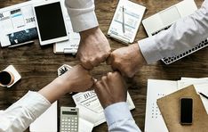 two people holding hands over a wooden table covered in papers and other office supplies on top of it