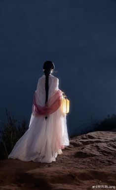 a woman in a long white dress holding a suitcase on top of a dirt hill