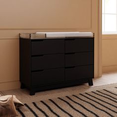 a baby crib in a room with beige walls and black drawers on the floor