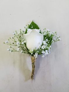 a white rose and baby's breath boutonniere on a white wall