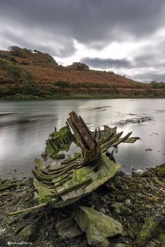 an old wooden boat sitting on top of a rocky beach next to the ocean under a cloudy sky