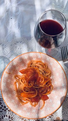 a white plate topped with spaghetti and sauce next to a glass of wine on top of a table