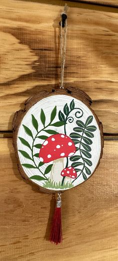 a wooden plaque with a mushroom and leaves painted on it, hanging from a string