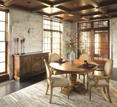 a dining room table with four chairs and a vase on top of it in front of two windows