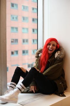 a woman with long red hair is sitting on a window sill and smiling at the camera