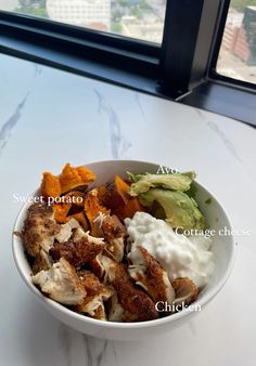 a white bowl filled with different types of food on top of a table next to a window