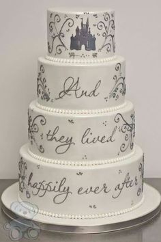 a white wedding cake with black writing on the bottom and castle in the middle, sitting on top of a table