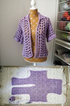 a purple crocheted jacket sitting on top of a table next to a mannequin