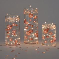 three glass vases with lights in them sitting on a table next to gold coins